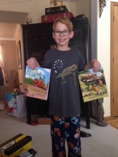 A boy stands holding his favorite curly-tail books by Elaine A. Powers.