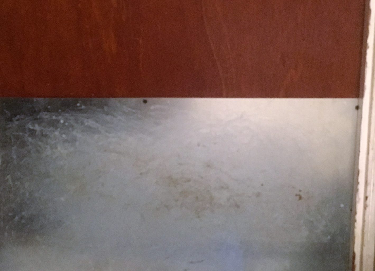 A silver-colored metal plate is installed across the bottom of a red-brown wooden door (to keep a Sulcata tortoise from digging through the door)