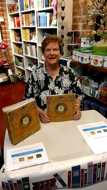 female author sitting at book signing table, books in the background