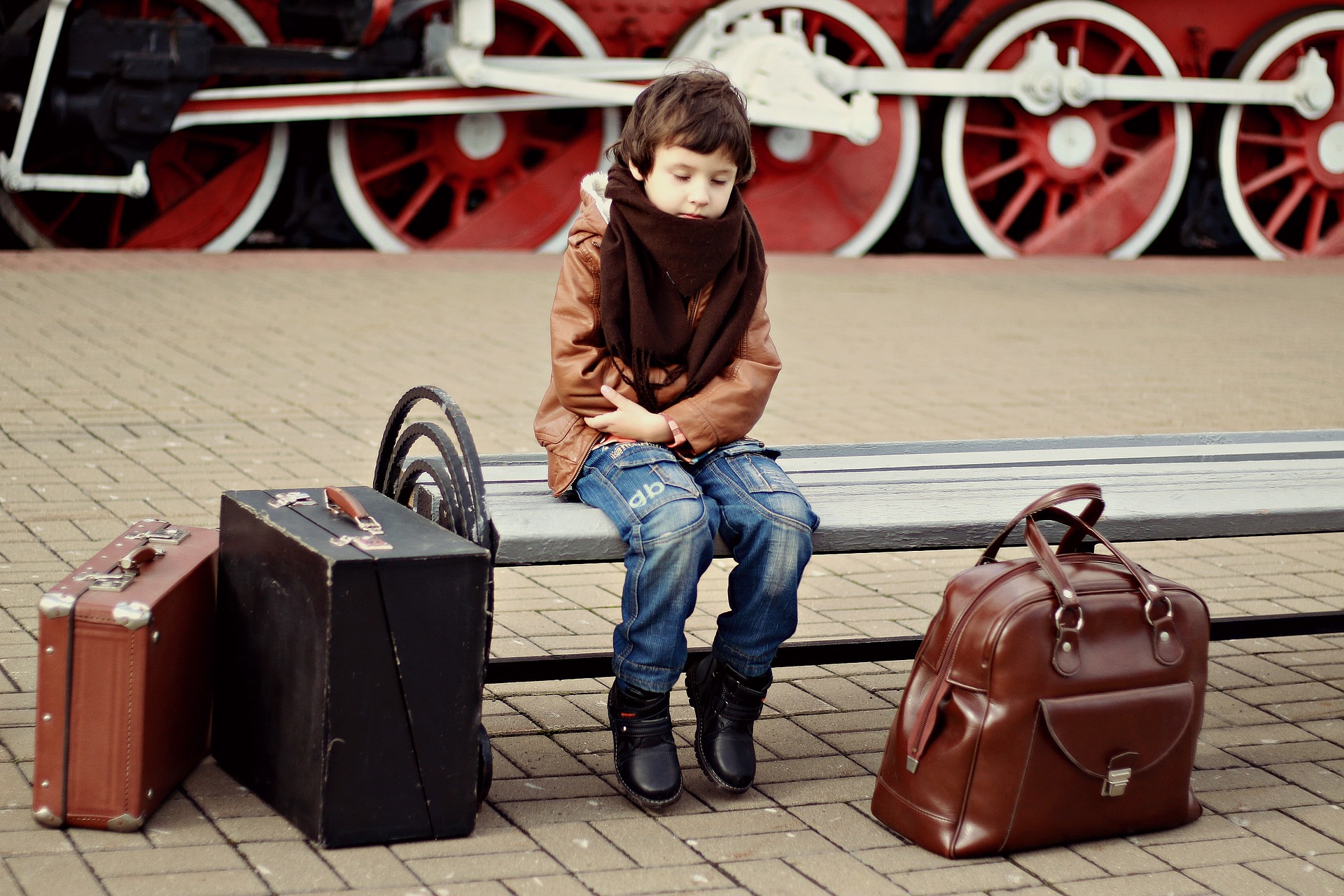 young child on train station bench near suitcases