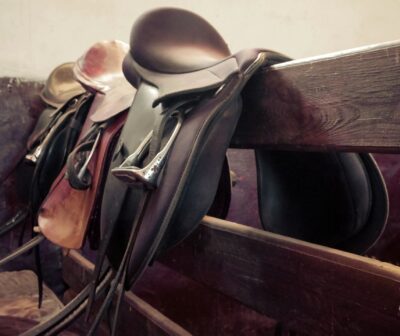 Three saddles lined up on a fence.