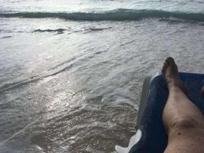 The edge of Elaine's leg resting on a beach chair as waves wash up all around.