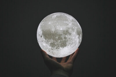 A hand extends in darkness holding a bright full moon.