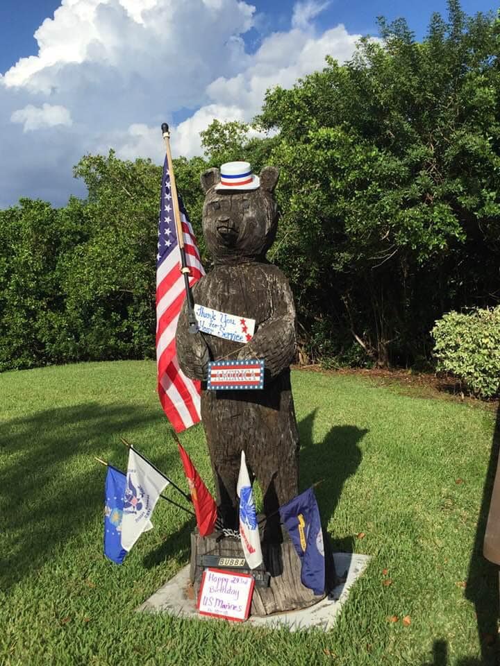 A large bear carved out of wood wearing a red, white and blue hat and carrying a US flag.