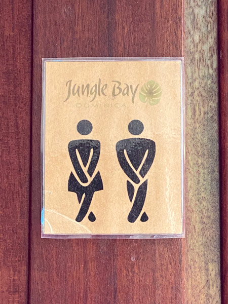 A bathroom sign that reads "Jungle Bay" and depicts two stick figures, one wearing a skirt with their legs twisted together, holding in their pee.
