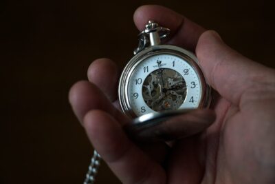 A hand holds a pocket watch, as if checking the time.