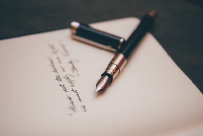 A fountain pen rests on a paper with a partial poem written on it.