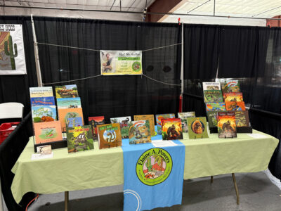 Elaine's table at the 2025 Tucson Reptile show. It has a green table cloth and all her children's books on display.