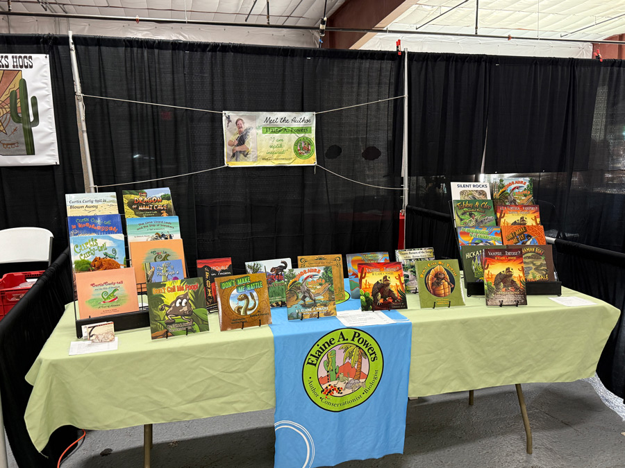 Elaine's table at the 2025 Tucson Reptile show. It has a green table cloth and all her children's books on display.