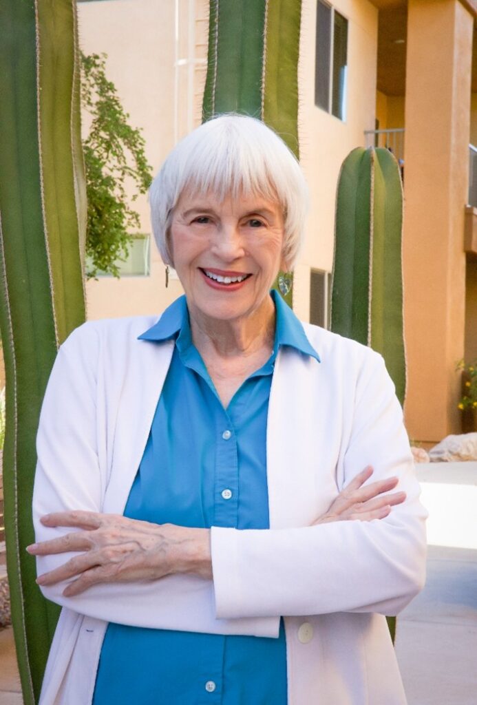 Janet McCormick is a white woman with short white hair, she is wearing white sweater and blue collar shirt.