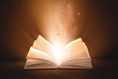 Open magic book with glow and flying butterflies on dark background.