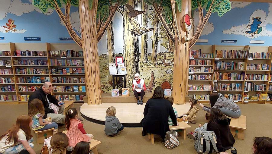 Janet sitting on a little stage, reading a picture book to a group of young children.